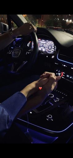 a person driving a car at night with their hand on the steering wheel and lights on