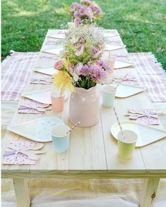 a wooden table topped with lots of plates and cups next to a vase filled with flowers