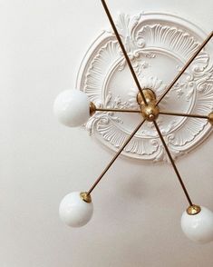 a ceiling light with five white balls hanging from it's center and four gold poles