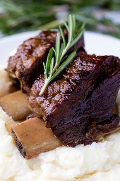 a plate with mashed potatoes and meat on it, garnished with rosemary