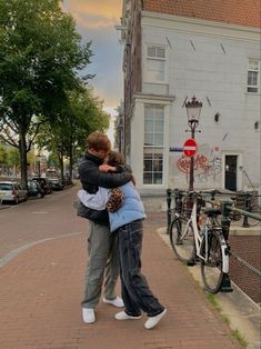 two people hugging each other on the sidewalk