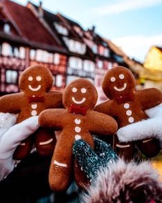 three gingerbread men are being held up by someone's hands in front of some buildings