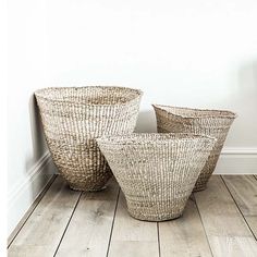 three woven baskets sitting on top of a wooden floor next to a white painted wall