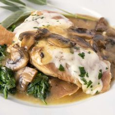 a white plate topped with meat covered in mushrooms and spinach on top of gravy