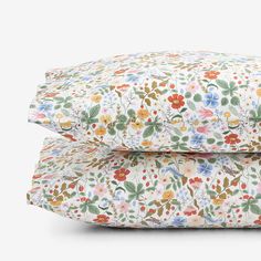 two pillows are stacked on top of each other, one is white and the other has multicolored flowers