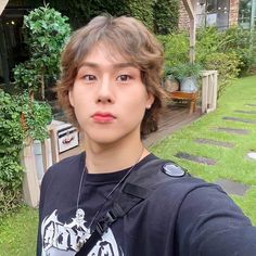 a young man standing in front of a house wearing a black t - shirt and holding a camera