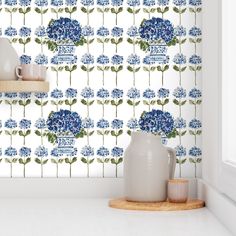 blue flowers are on the wall next to a white vase and some cups in front of it