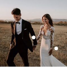 a man and woman walking through a field holding hands