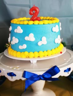 a blue and yellow birthday cake with a red number two on it's top