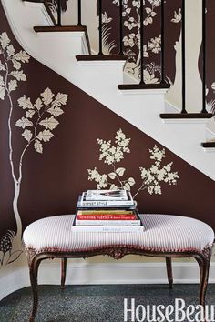 a white bench sitting under a stair case next to a wall with flowers on it