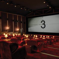 an empty movie theater with red chairs and candles on the seats, in front of a large screen