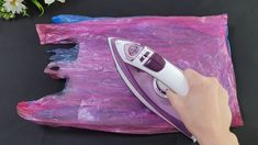 a person is using an electric iron on some plastic bags with flowers in the background