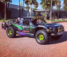 the monster truck is parked in front of some palm tree's on a brick road