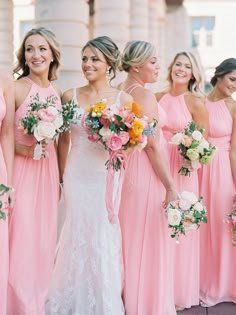 a group of women standing next to each other wearing pink dresses and holding bouquets