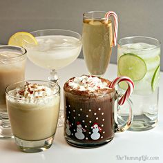 various drinks are lined up on a white table with candy canes and lime slices