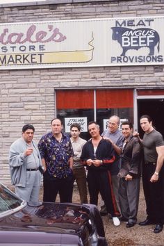 a group of people standing in front of a building with a car parked outside it