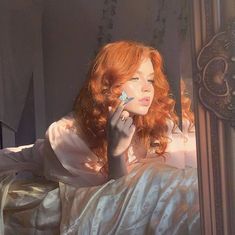 a woman with red hair sitting on a bed looking at her reflection in the mirror