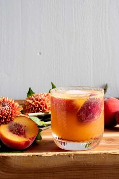 a glass filled with liquid sitting on top of a wooden table next to peaches