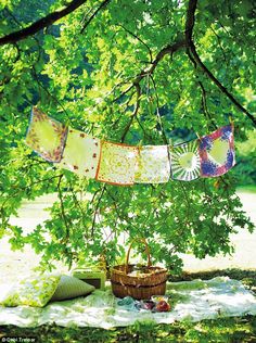 an outdoor area with blankets, pillows and a basket on the ground under a tree