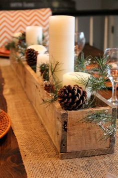 a wooden box filled with pine cones and candles on top of a dining room table