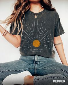 The "Be The Light Mathew 5:14 Sunburst Vintage Bible Verse Christian Celestial Comfort Colors T-shirt" is a beautifully crafted, comfortable shirt featuring an inspirational biblical verse and celestial sunburst design. Its unique blend of faith and style makes it a standout addition to any wardrobe or a meaningful gift. * Q U I C K * F A C T S * ✺ 100% preshrunk cotton ✺ Wash (inside out) and dry normally (on cool for best results) * S I Z I N G * ✺ Sizing is unisex so runs like men's, though not overly large ✺ Most women find their typical size works best, since they are meant to fit a touch loose ✺ For an oversized look size up 1-2+ sizes! ✺ Size guide and fit: SIZE / WIDTH / LENGTH (in inches) S W18" L28" M W20" L29" L W22" L30" XL W24" L31" 2XL W26" L32" 3XL W28" L33" * H O W * T O * Christian Aesthetics, Mathew 5, Vintage Bible, Comfort Colors Tshirt, Be The Light, Boho Shirt, Sun Shirt, Girls Camp, Beach T Shirts