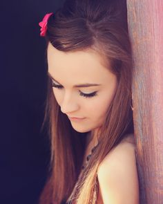 a woman with long hair leaning against a wooden wall