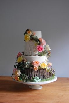 a three tiered wedding cake with flowers on the top and bottom, sitting on a wooden table