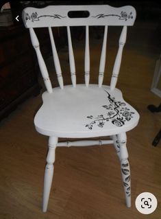 a white chair painted with black flowers and vines on it's back legs, sitting in a living room