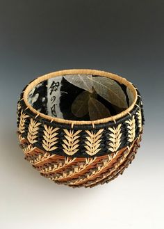 a black and white basket with leaves on the inside is sitting in front of a gray background