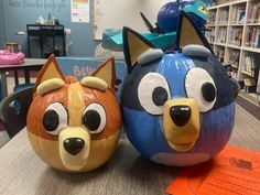 two pumpkins decorated to look like cartoon characters sitting on a table in a classroom