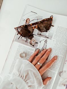 a woman's hand with sunglasses on top of an open book