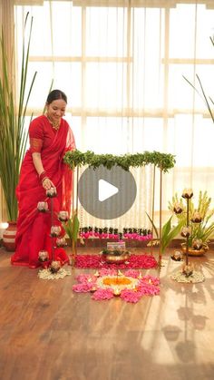 a woman in a red sari standing next to a flower arrangement on a wooden floor