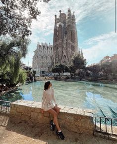 a woman sitting on a ledge looking at the water in front of a building with towers