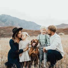 a man, woman and two children are sitting in the grass with a dog on their lap