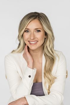 a woman with long blonde hair wearing a white blazer and smiling at the camera