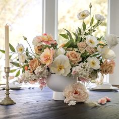 a vase filled with lots of flowers on top of a wooden table next to two candles