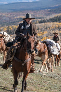 a man riding on the back of a brown horse next to other horses in a field