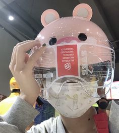 a person wearing a face mask with ears and nose rings on their head while holding up a clear plastic object