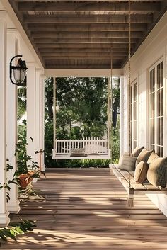 a porch with two white swings and pillows hanging from it's sides, along with potted plants on either side