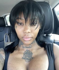 a woman with tattoos on her chest sitting in the back seat of a car and looking at the camera