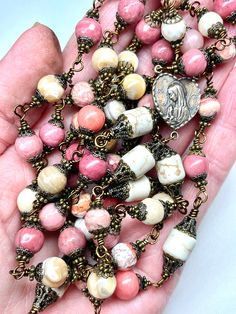 "There are 59 total beads. This rosary has a 1.75 Inch (44 mm) TRUE BRONZE   beautifully detailed  Crucifix, a True Bronze Mary Center on front with the the Sacred Heart of Jesus on the other side.  There are fifty-three 8 mm Beads, and 6 larger Cream Color Barrel Beads for the Pater or \"Our Father\" beads. There are a total of 236 bronze bead caps in this rosary, WOW! Your rosary will come nicely packaged in an organza pouch with a \"How To Pray The Rosary\" included. Beads included are a mixt Artisan Handmade Rosary, Colorful Beads Rosary As Gift, Spiritual Rosary With Spacer Beads, Pink Healing Rosary With 8mm Beads, Handmade Pink Rosary For Healing, Pink Rosary With 8mm Round Beads, Spiritual Round Beads Rosary For Jewelry Making, Spiritual Rosary Bracelet With Round Beads For Jewelry Making, Handmade Pink Rosary With Round Beads