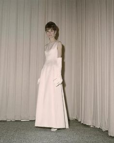 a woman in a long white dress standing next to a curtain with her hands on her hips