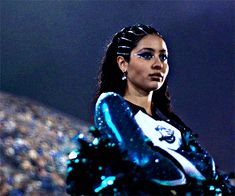 a woman in blue and white outfit standing next to a stadium filled with people at night