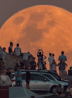 the full moon is setting behind some people