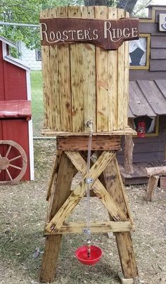 a wooden water pump sitting in the grass next to a red bucket on top of it