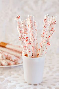 a cup filled with candy canes sitting on top of a white tablecloth next to a slice of cake