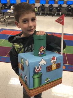 a young boy standing in front of a cake shaped like a mario kart box