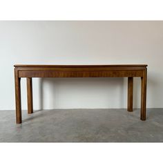 a long wooden table sitting on top of a cement floor next to a white wall