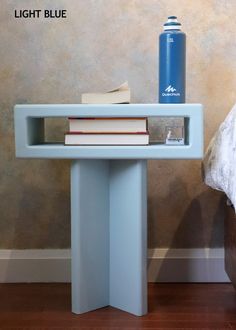 a blue table with books and a water bottle on it next to a white bed