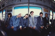 four men in suits are sitting on a bus